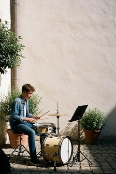 Young man playing a drum kit outdoors in a courtyard