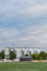 Complex of grain silos with roung green wheat field under cloudy sky. Copy space.  © kyrychukvitaliy