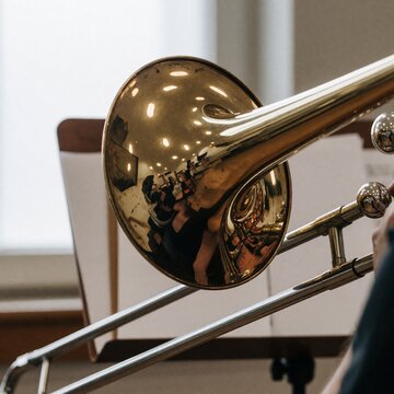 Close-up of a brass trombone bell reflecting a choir