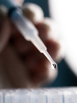 Macro shot of a pipette dispensing a liquid drop in a laboratory