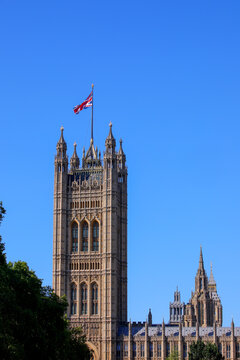Victoria Tower at Palace of Westminster with Union Jack flag flying against clear blue sky in London UK