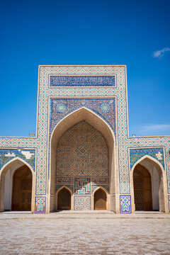 Symmetrical view of historic Islamic architecture in Bukhara, Uzbekistan, featuring a monumental pointed arch decorated with intricate blue and turquoise mosaic tiles, geometric patterns