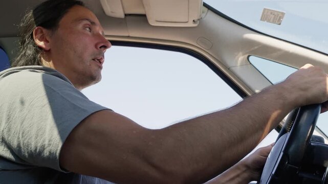 Low-angle close-up of attentive male driver checking surroundings while holding steering wheel, with driver, man, hand, steering detail, showing wheel, car, interior, profile context
