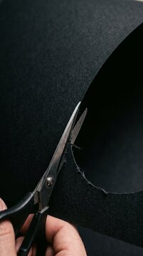 A pair of scissors cutting a sharp curve into a Halloween mask making black paper