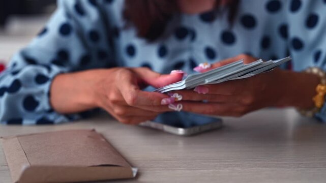 Female investor holds cash when managing investment decisions, executing investment strategy, placing cash beside brown paper envelope, securing personal investment funds.