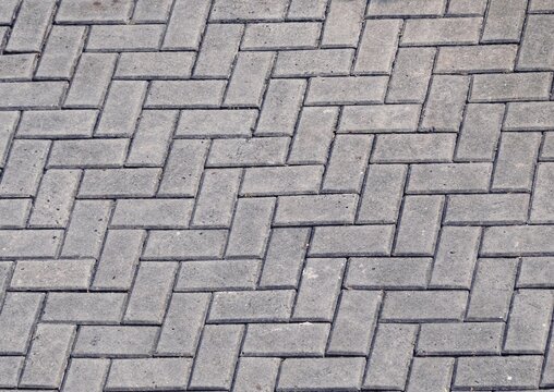 Grey interlocking paving blocks laid in a herringbone pattern texture 