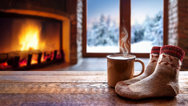 Mug of hot cocoa by cozy fireplace with blurred snowy window background banner.
