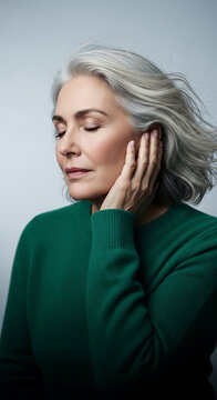 Close-up portrait of a mature woman with silver hair, her hand touching her face, conveying a sense of peace and introspection, ideal for lifestyle or wellness themes