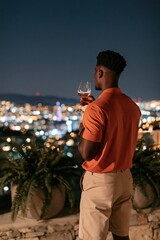 Obraz premium Man on rooftop terrace with wine glass overlooking city skyline at night for lifestyle background and evening relaxation scene