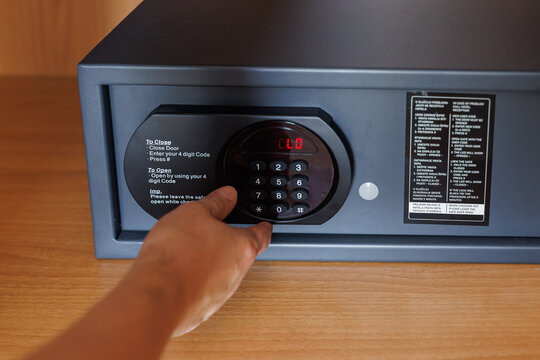 Finger presses numeric keypad buttons to lock an electronic hotel safe containing personal valuables. Concept of access control, safe operation, theft prevention, privacy and secure travel storage.