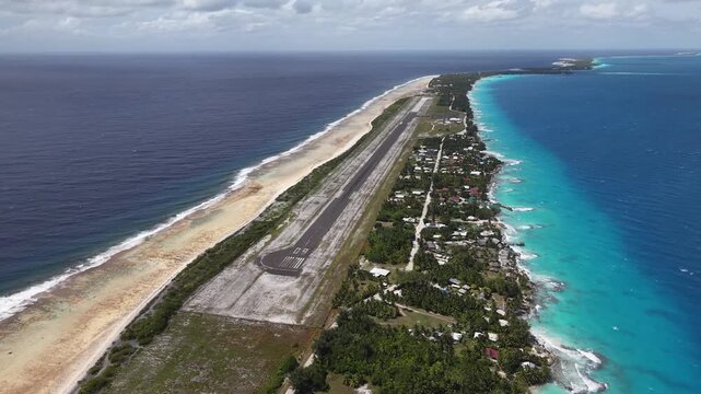 Aerial pan down shot revealing the remote asphalt runway of Rangiroa Airport flanked by the deep blue Pacific Ocean and an exotic turquoise lagoon