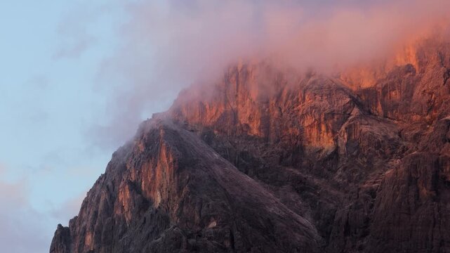 Aerial view of the rugged Dolomites mountain peaks illuminated by golden hour light with soft clouds drifting over the rocky slopes in Primiero San Martino di Castrozza, Trentino-Alto Adige, Italy.