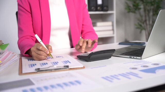 Accounting for Success: A focused professional analyzes financial reports at her desk, utilizing a calculator and laptop to manage data. The scene emphasizes diligent work and financial management.