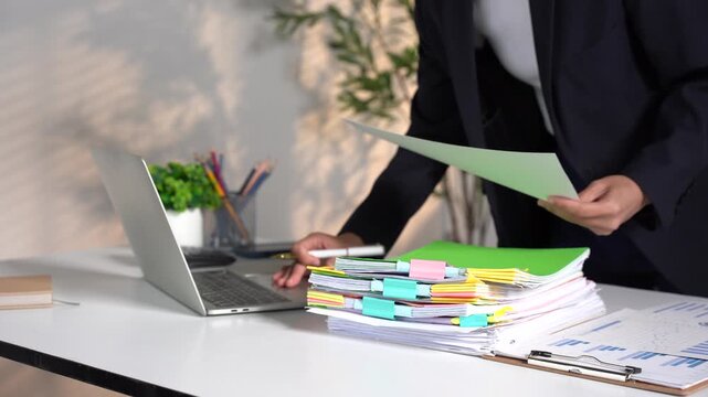 Businesswoman hands working in Stacks of paper files for searching and checking unfinished document achieves on folders papers at busy work desk office.	