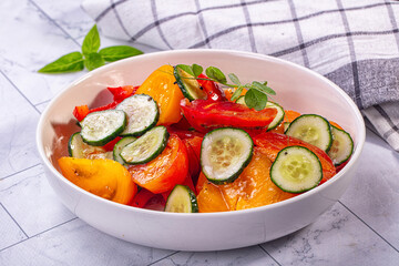 Fresh cucumber and tomato salad with bell pepper in white bowl on marble surface
