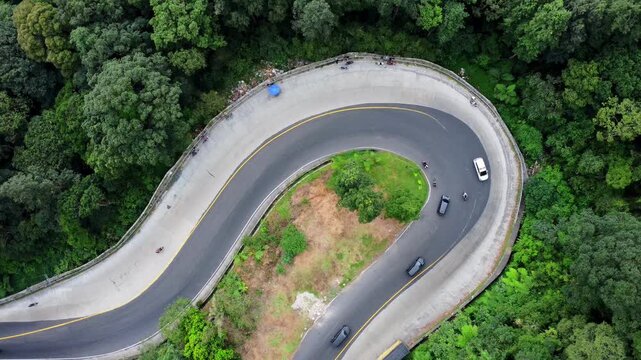 Aerial view of a winding road through a lush forest with vehicles navigating a sharp hairpin turn in Sibolangit, North Sumatra, Indonesia.
