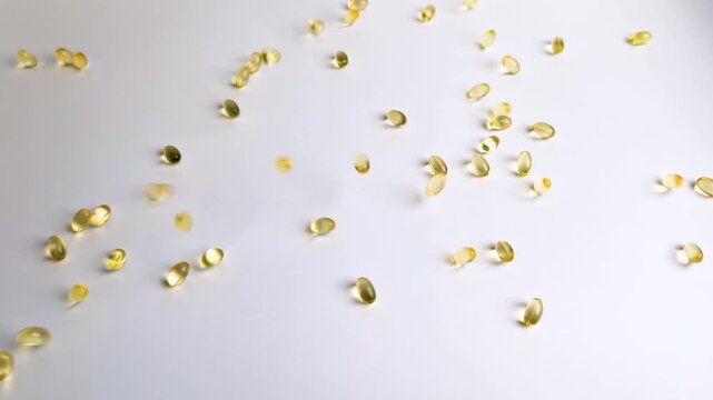 Yellow golden gelatin softgel capsules falling and bouncing on smooth white surface Concept of healthcare dietary supplements fish oil vitamin D3, omega 3 fatty acids nutrition pharmaceutical medicine