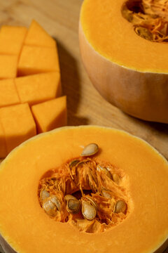 Fresh butternut squash halves showing seeds and fibrous pulp beside diced orange cubes on a wooden board. Raw seasonal vegetable prepared for cooking.