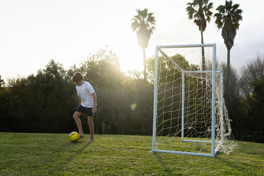 teenage boy practicing his soccer moves on field at sunset