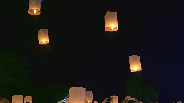 Beautiful floating lanterns rising into the dark night sky during Yee Peng Festival in Thailand. People releasing traditional paper lamps for luck and celebration.