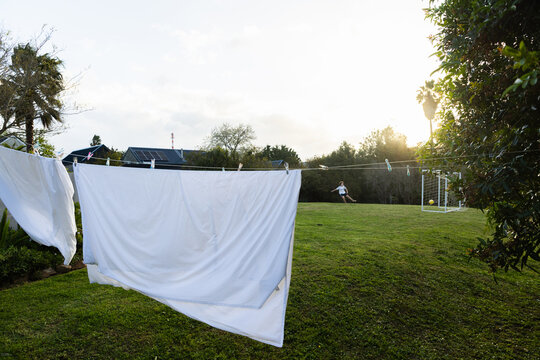 teenage soccer player visible through white sheets drying on clothes line at sunset