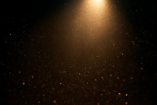 Golden dust particles floating in a beam of light on a black background