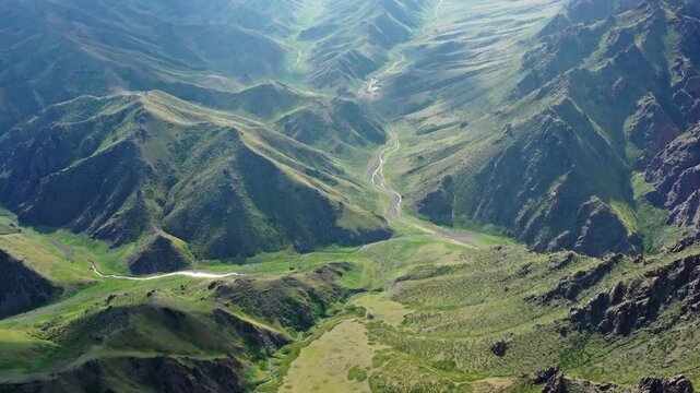 Aerial view of a winding river flowing through a lush green valley surrounded by rugged mountain slopes in Mongolia.