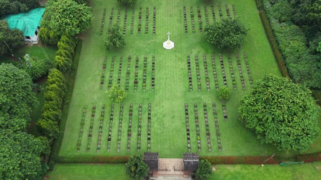 Aerial view of the historic Chittagong War Cemetery featuring rows of gravestones and a central stone cross set within lush green lawns in Chittagong, Chittagong Division, Bangladesh.