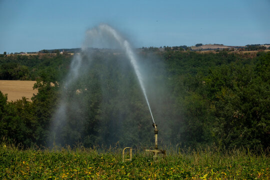 Agricultural irrigation sprinkler spraying water over farmland with forested hills in the background, Gers, Saint Georges, France