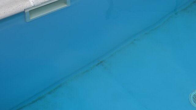 Tracking shot of dirty blue residential swimming pool showing algae and dirt accumulated on bottom
