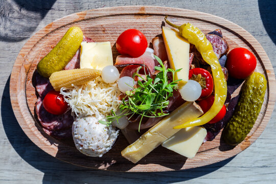 A top-down, high-angle view of a traditional Austrian Brettjause in Tyrol served on a rustic oval wooden platter over a sunlit wooden table.