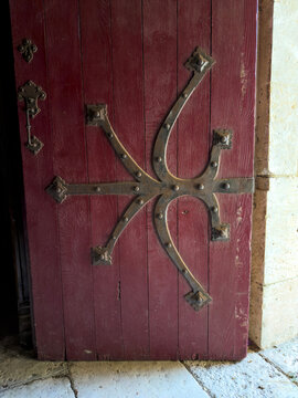 Ornate wrought-iron star-shaped hinges decorating a red wooden church door, Gers, Sarrant, France
