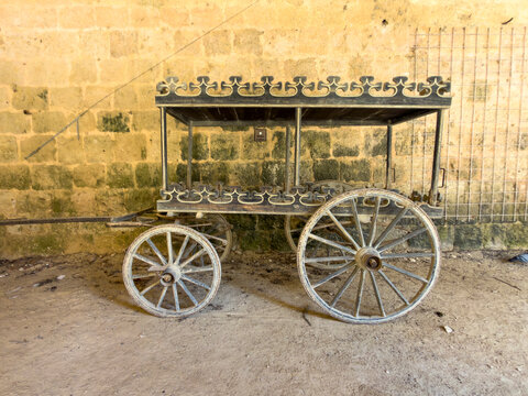 Antique horse-drawn cart with cast-iron fretwork trim parked against a stone wall, Gers, La Romieu, France