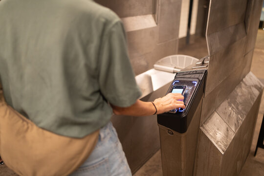 Person tapping a smartphone to a digital reader at a subway turnstile, making a contactless payment for public transportation access, representing modern urban commuting and nfc technology