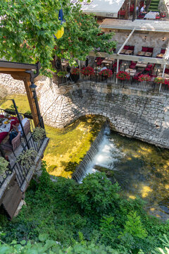 Mostar, Federation of Bosnia, Bosnia and Herzegovina - 22 June 2025: View of a restaurant terrace overlooking a small waterfall on the Radobolja river, featuring stone walls and lush greenery.