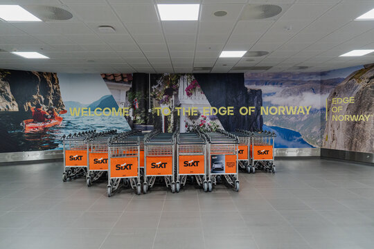August 15, 2026, Stavanger, Norway - Sixt luggage trolleys in front of 'Welcome to the Edge of Norway' mural at Stavanger Airport