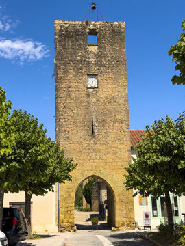 Fortified stone gate tower with a clock, framed by trees on the village square, Gers, Bassoues, France