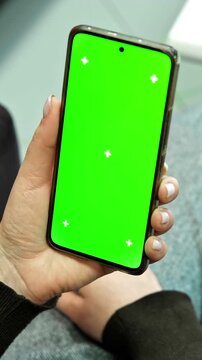 Female hand holding smartphone vertically with green screen chroma key blank display and tracking markers. Close up of woman using mobile phone template mockup for application design. Vertical video