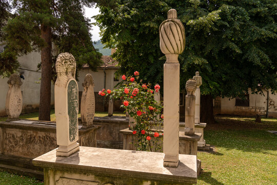 Sarajevo, Federation of Bosnia, Bosnia and Herzegovina - 16 June 2025: View of historic Ottoman stone tombstones with carved finials in a cemetery with trees and roses.
