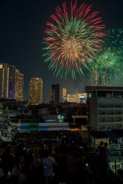 Bangkok, Thailand - 31 December 2025: View of New Year fireworks at Iconsiam lighting up the night sky over the city skyline with a crowd of people watching from a rooftop.