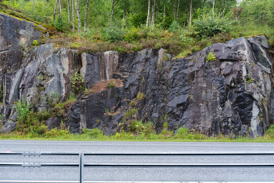 Rugged rock cliff side with green forest and empty road view background