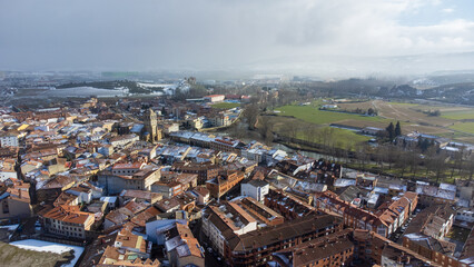 Fototapeta premium Elevated view over the historic old town center of Aguilar de Campoo with snow-dusted rooftops under low misty clouds on a sunny winter day. Aguilar de Campoo, Castile and Leon, Spain.