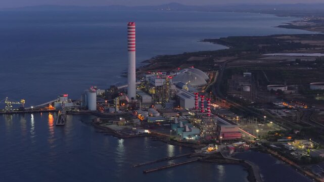Aerial view of the Centrale Termoelettrica Torrevaldaliga Nord power plant with its iconic striped chimney along the coast at twilight in Civitavecchia, Lazio, Italy.
