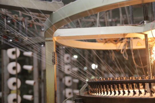 Lahore, Punjab, Pakistan - 02 October 2024: View of a circular knitting machine in operation at the Quaid-e-Azam Industrial Estate, with threads being fed into the loom in a textile factory.
