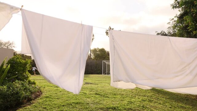 teenage boy practicing kicking soccer ball through white sheets drying on a clothes line at sunset