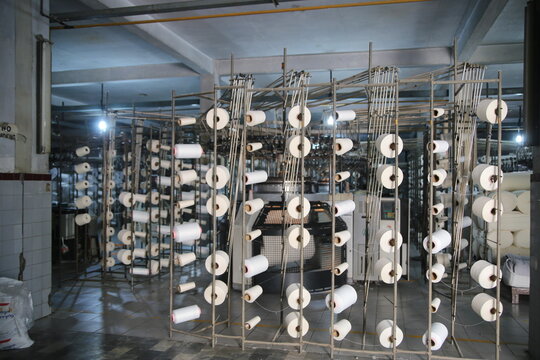 Lahore, Pakistan - 02 October 2024: View of Quaid-e-Azam Industrial Estate showing textile machinery with numerous white yarn spools in a factory setting.