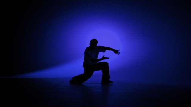 Hip hop dancer striking a dramatic pose under blue studio lights