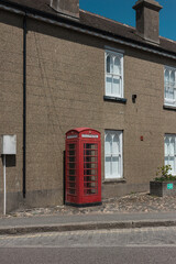 A red telephone box against a pebbledash terrace in a Cornish village, with white shuttered windows and a cobbled verge. © Victor