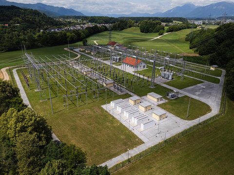 Drone view shows a battery energy storage facility adjacent to electrical infrastructure in a green landscape with mountains.