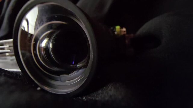 Cinematic extreme close-up of a dark optical cylindrical lens barrel resting on a black textured surface with violet glass reflections and internal mechanisms.